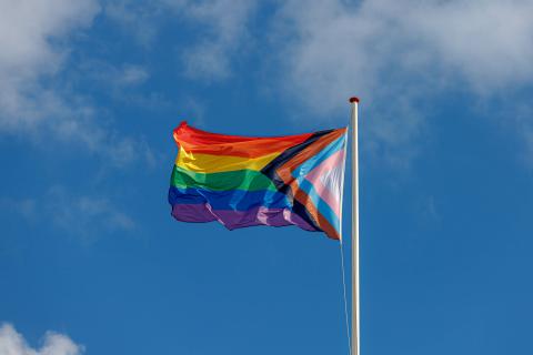 The pride flag blowing in the wind in front of the blue sky. 