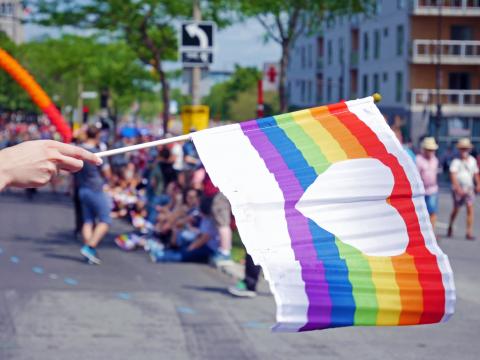 A rainbow flag with a white heart at its center waves in front of a crowd.