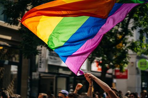 A rainbow fag above the heads of many people in a parade. 