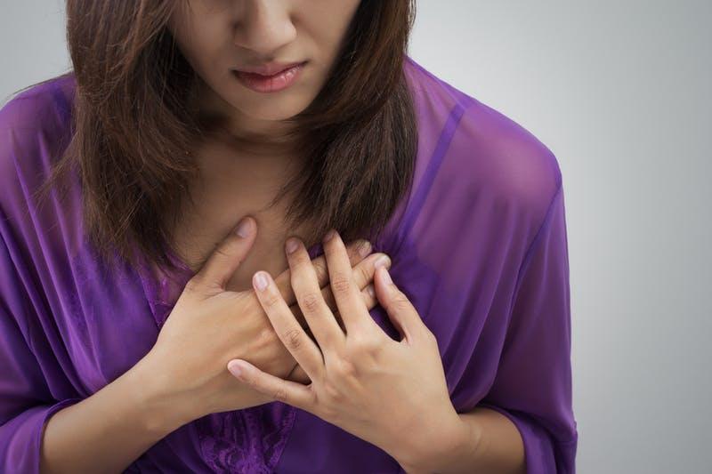 Close-up of a woman's hands holding her chest.