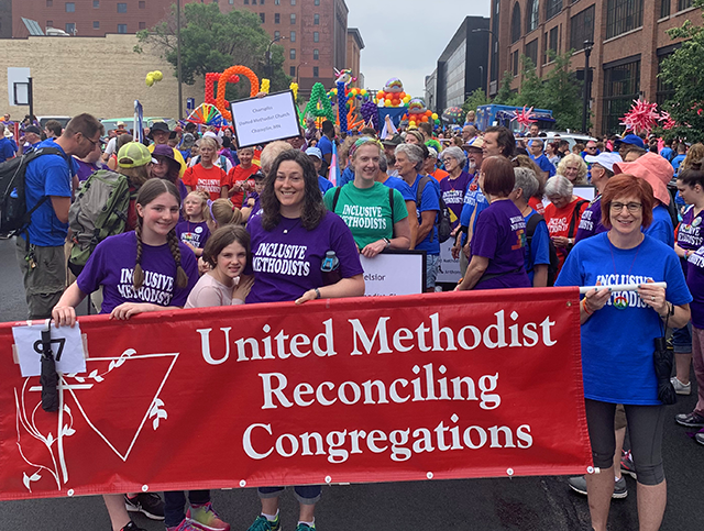 Several marchers stand wearing shirts reading "Inclusive Methodists" and holding a red banner which reads "United Methodist Reconciling Congregations."